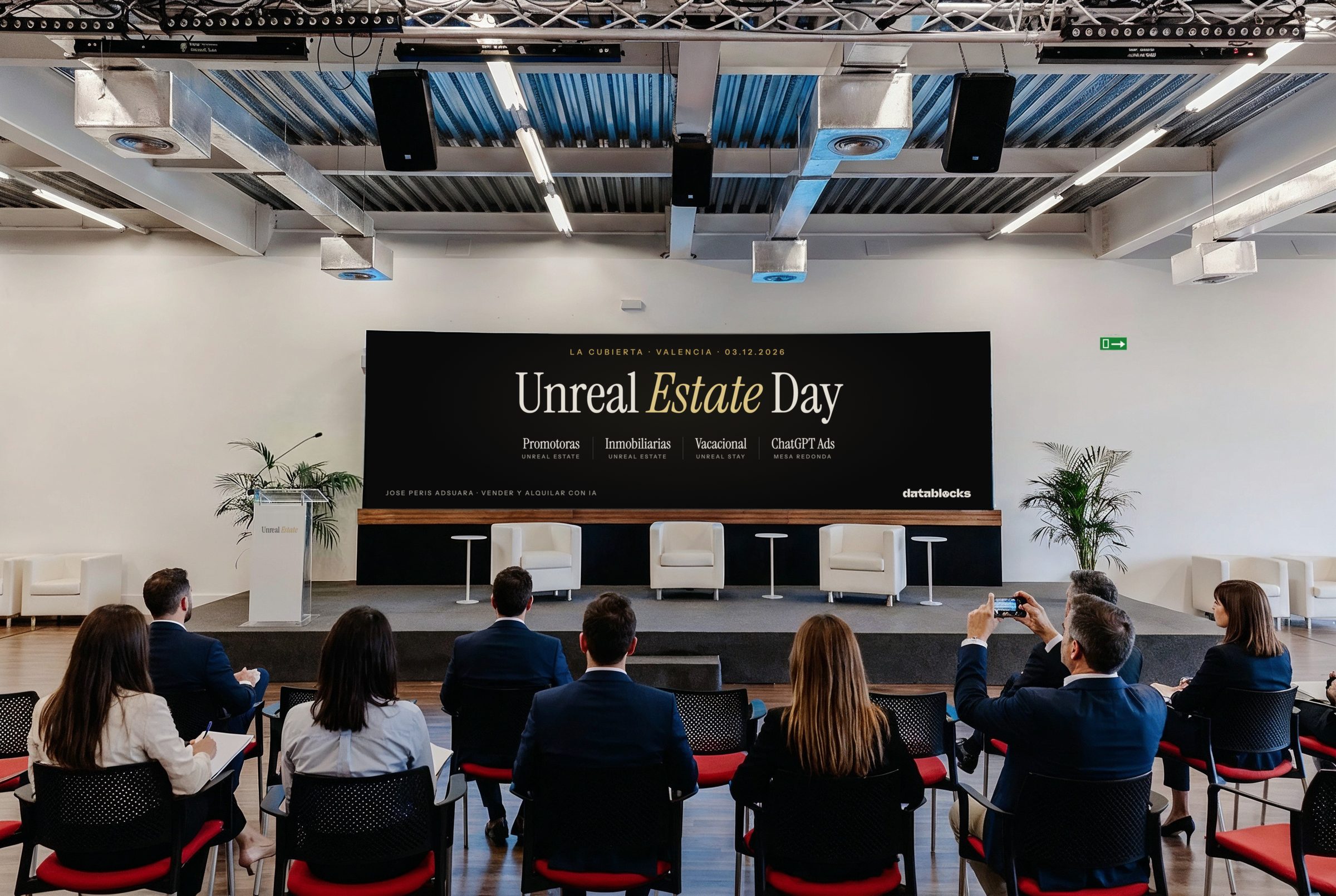 El escenario de La Cubierta con la pantalla LED mostrando Unreal Estate Day: Promotoras, Inmobiliarias, Vacacional y ChatGPT Ads, el atril preparado y el público en la sala